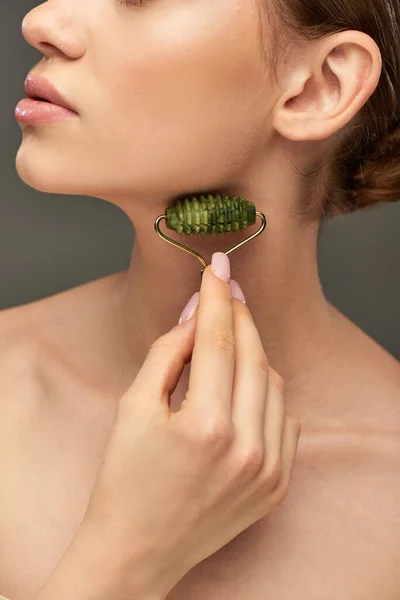 Femme recadrée avec peau parfaite massage visage avec rouleau de jade vert sur fond gris, soins de la peau — Photo de stock