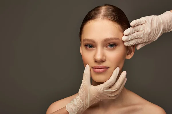 Estheticians in medical gloves examining face of woman on grey background, dermatology concept — Stock Photo