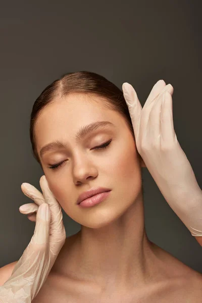 Estheticians in medical gloves touching face of woman on grey background, dermatology concept — Stock Photo