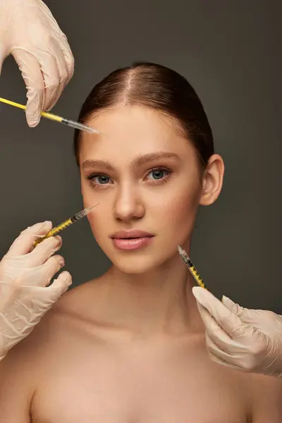 Estheticians in medical gloves holding syringes near young woman on grey background, collagen — Stock Photo