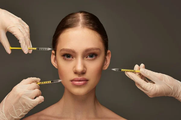 Esteticistas em luvas médicas segurando seringas perto de mulher jovem em fundo cinza, procedimento — Fotografia de Stock