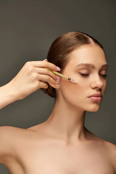 Pretty young woman holding syringe near face on grey background, skin rejuvenation concept — Stock Photo