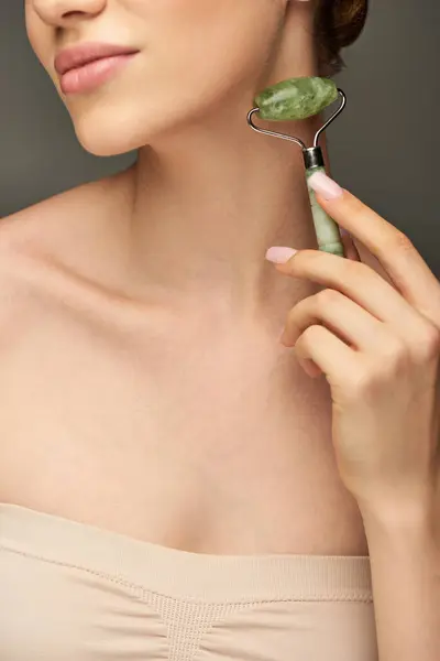 Vue recadrée de la femme faisant un massage du cou avec rouleau de jade sur fond gris, rajeunissement — Photo de stock