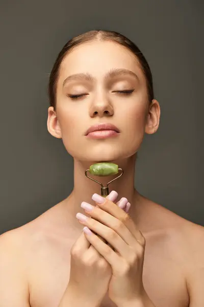 Ritratto di giovane donna che fa massaggio del collo con rullo di giada verde su sfondo grigio, auto-cura — Foto stock