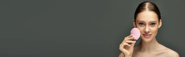 Junge Frau mit Reinigungsbürste auf grauem Hintergrund, Beauty-Gadget und Hautpflege-Banner — Stockfoto