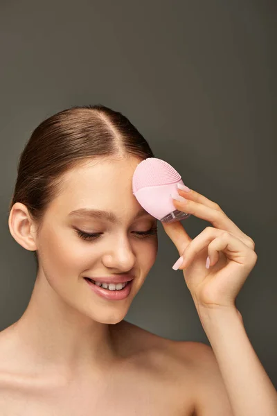 Mulher feliz segurando escova de limpeza no fundo cinza, gadget de beleza e conceito de cuidados com a pele — Fotografia de Stock