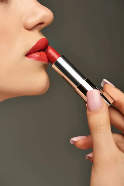 Vue recadrée de jeune femme glamour appliquant rouge à lèvres sur fond gris, beauté et maquillage — Photo de stock