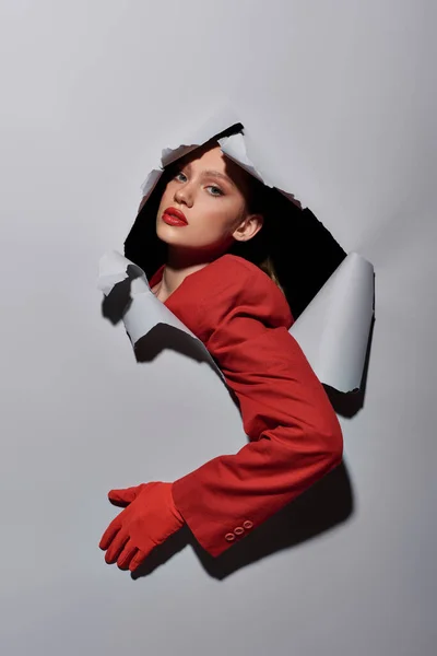 Attraktive Frau mit rotem Ärmel und Handschuh, die durch Loch in grauem Hintergrund bricht, konzeptionell — Stockfoto
