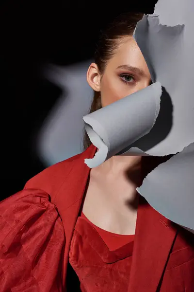 Beautiful young woman with bright red lips posing near torn grey paper and looking at camera — Stock Photo