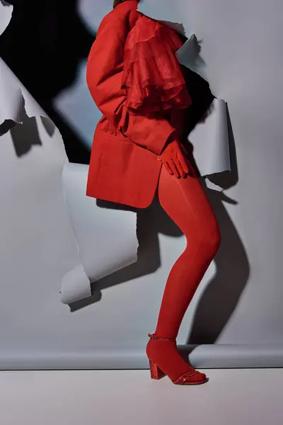 Vista recortada de la mujer joven de moda en traje rojo rompiendo a través de fondo gris con agujero - foto de stock