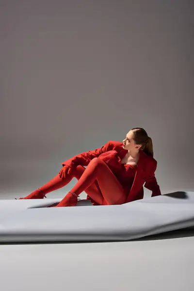 Comprimento total de elegante jovem mulher em roupa vermelha com luvas e blazer posando em fundo cinza — Fotografia de Stock