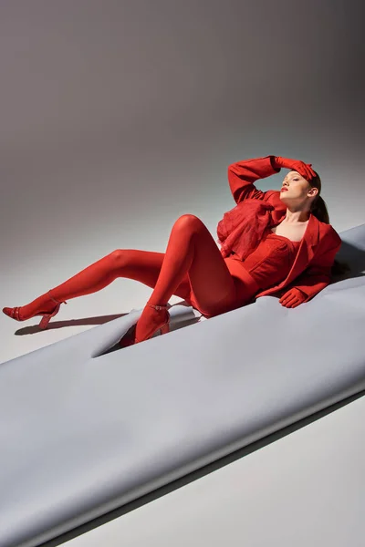 Comprimento total de modelo muito jovem em roupa vermelha com luvas e blazer posando em fundo cinza — Fotografia de Stock