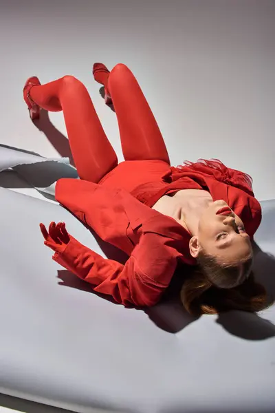 Full length of stylish young model in red outfit with gloves and blazer posing on grey background — Stock Photo