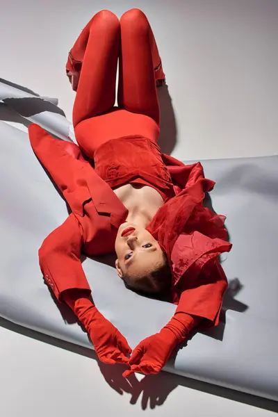 Junges Model in rotem Outfit mit Strumpfhosen posiert auf grauem Hintergrund liegend, schaut in die Kamera — Stockfoto