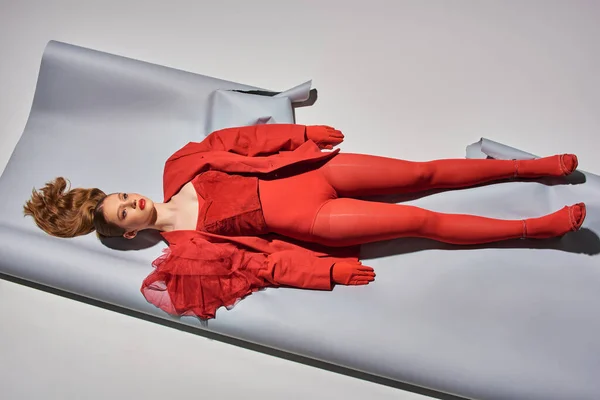 Vista superior de jovem modelo em roupa vermelha deitado sobre fundo cinza, mulher agindo como uma boneca — Fotografia de Stock