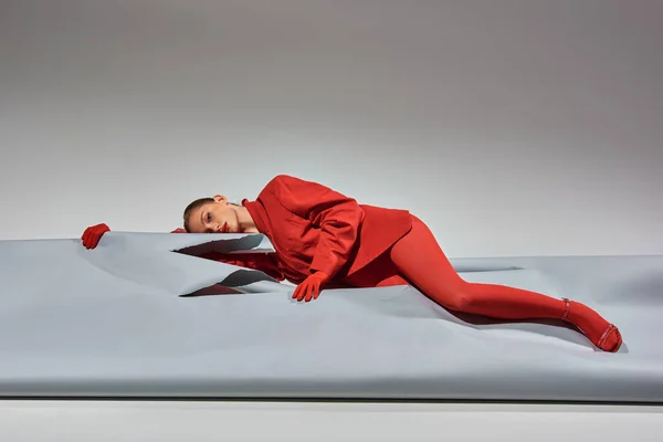 Young woman in red attire with gloves and tights lying near ripped paper on grey background — Stock Photo