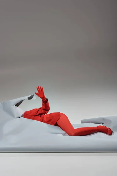 Cropped model in red attire with gloves and tights lying near ripped paper on grey background — Stock Photo