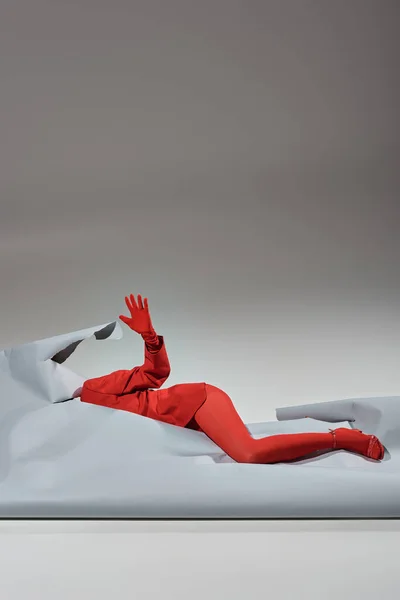 Modelo recortado en traje rojo con guantes y medias que yacen cerca de papel rasgado sobre fondo gris - foto de stock
