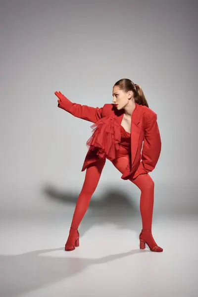 Glamourosa jovem mulher em traje vermelho com saltos altos e meias brilhantes gesticulando em fundo cinza — Fotografia de Stock