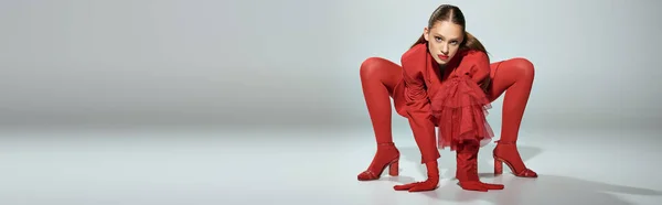 Знамя гламурной модели в красной одежде с высокими каблуками и яркими колготками, позирующими на сером фоне — стоковое фото