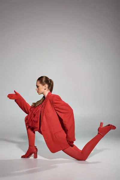 Stylisches Model in roter Kleidung mit Handschuhen und Strumpfhosen gestikulierend und posierend auf grauem Hintergrund — Stockfoto