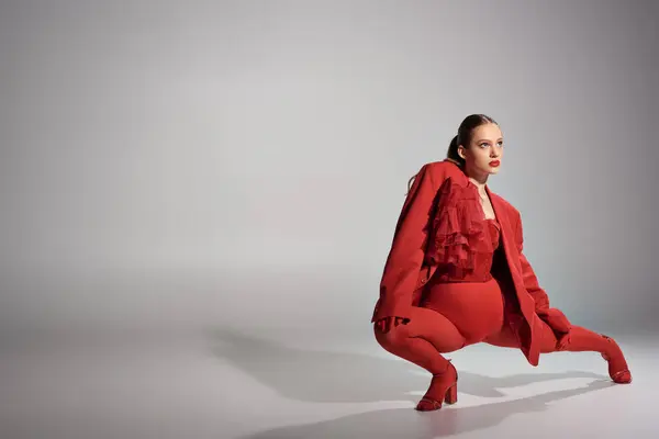 High fashion model in stylish red outfit with tights and high heels posing on grey background — Stock Photo