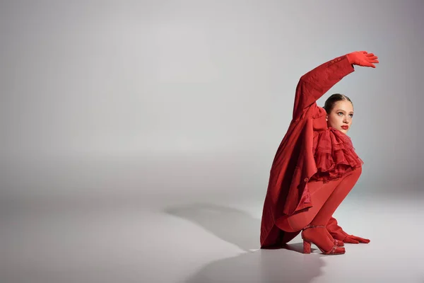 High Fashion junges Model in rotem stylischem Outfit posiert mit erhobener Hand auf grauem Hintergrund — Stockfoto