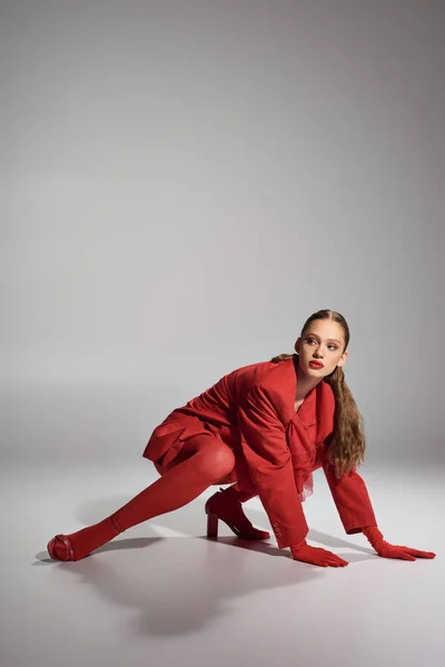 Висока модна молода модель в червоному стильному вбранні, дивлячись далеко, позуючи на сірому фоні — стокове фото