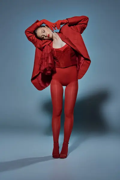 Modello alla moda con gli occhi chiusi in abito rosso in piedi in posa insolita su sfondo grigio — Foto stock