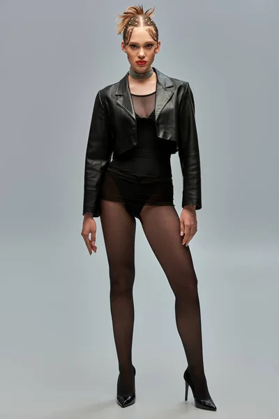 Stylish young woman with pearls in hair posing in leather jacket and black tights on grey background — Stock Photo