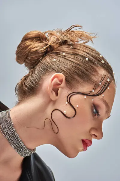 Seitenansicht einer hübschen jungen Frau mit trendigen Perlstiften im Haar und roten Lippen, die vor grauem Hintergrund posiert — Stockfoto