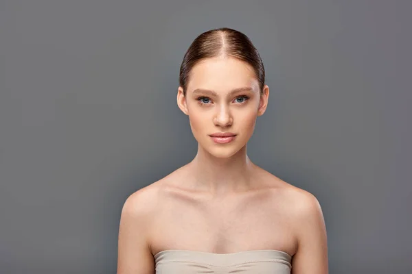 No makeup look, beautiful young woman with bare shoulders looking at camera on grey background — Stock Photo