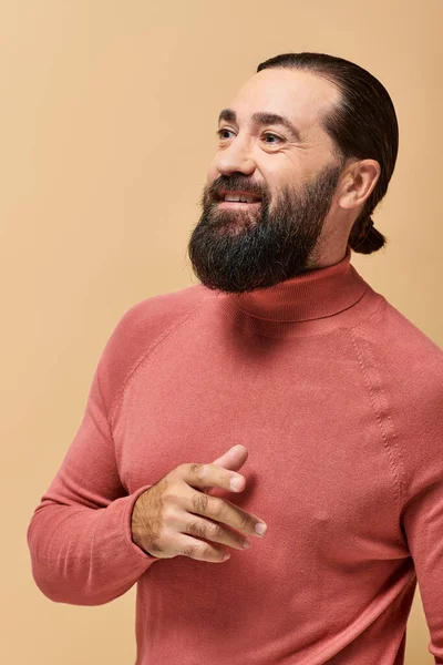 Uomo contento con la barba in maglione collo alto rosa sorridente allegramente sullo sfondo beige — Foto stock