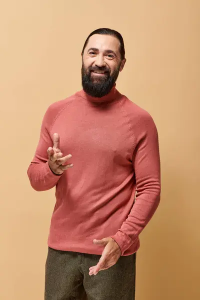 Счастливый человек с бородой в розовой водолазке свитер весело улыбается на бежевом фоне, радость — стоковое фото