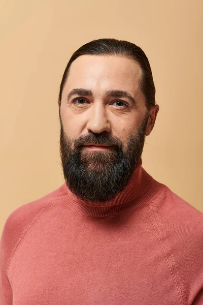 Portrait, homme sérieux et beau avec barbe posant en pull col roulé rose sur fond beige — Photo de stock