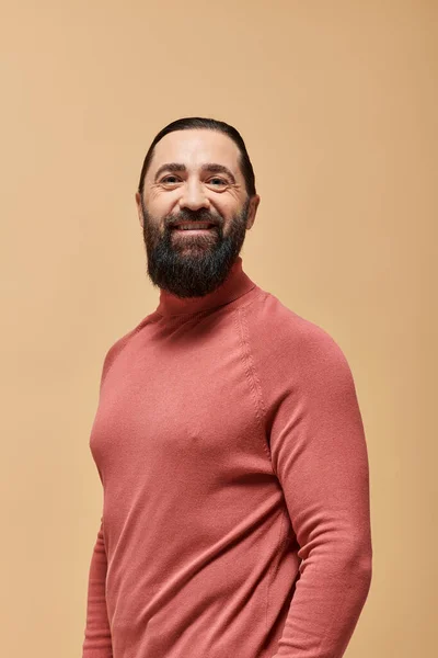 Happy man with beard in pink turtleneck jumper smiling cheerfully on beige backdrop — Stock Photo