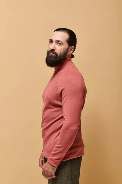 Portrait, bel homme sérieux avec barbe posant en pull col roulé rose sur fond beige — Photo de stock