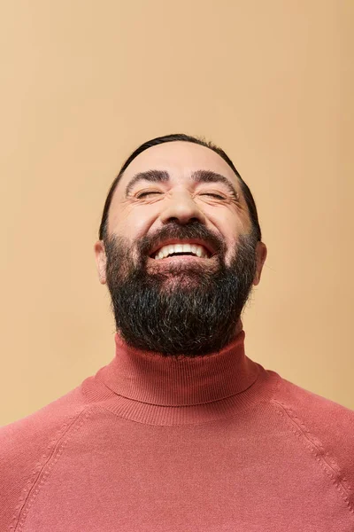 Smiling man with beard in pink turtleneck jumper smiling cheerfully on beige backdrop — Stock Photo