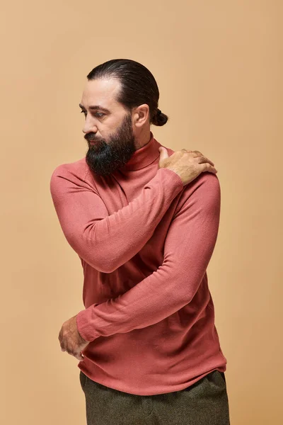 Ritratto, potente bell'uomo con la barba in posa rosa maglione collo alto su sfondo beige — Foto stock