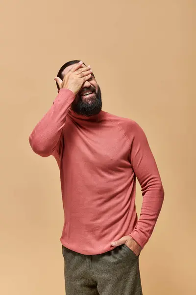 Homem feliz com barba em rosa gola alta jumper sorrindo alegremente no fundo bege — Stock Photo