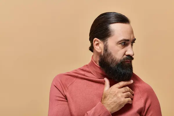Porträt eines gutaussehenden Mannes mit Bart, der im Rollkragenpullover auf beigem Hintergrund posiert, ernst — Stockfoto