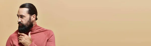 Sério e bonito homem com barba posando em rosa gola alta jumper no fundo bege, banner — Fotografia de Stock