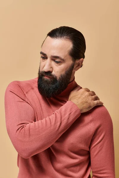Porträt, seriöser, gutaussehender Mann mit Bart posiert in rosa Rollkragenpullover auf beigem Hintergrund — Stockfoto