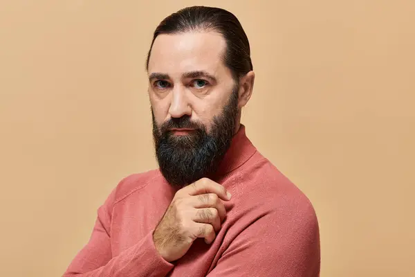 Portrait of good looking serious man with beard posing in pink turtleneck jumper on beige backdrop — Stock Photo