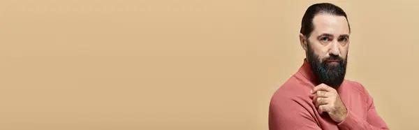 Portrait, homme sérieux et beau avec barbe posant en pull col roulé rose sur beige, bannière — Photo de stock