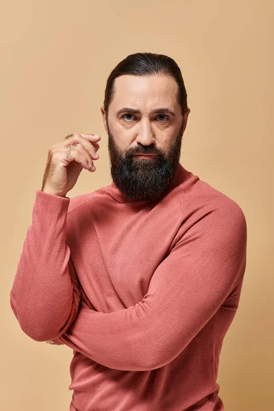 Uomo serio e bello con barba in posa rosa maglione dolcevita su sfondo beige, ritratto — Foto stock