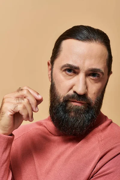 Handsome serious man with beard posing in pink turtleneck jumper on beige background, portrait — Stock Photo