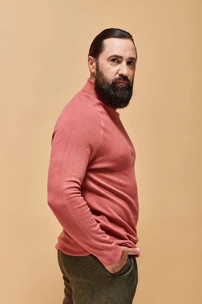 Homem bonito e sério com barba posando em rosa gola alta jumper no bege, retrato — Fotografia de Stock