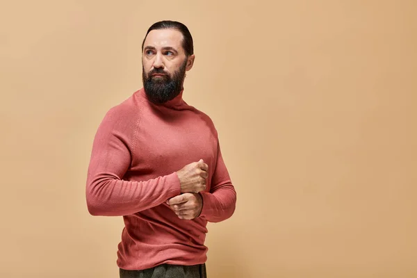 Good looking and serious man with beard posing in pink turtleneck jumper on beige backdrop, portrait — Stock Photo