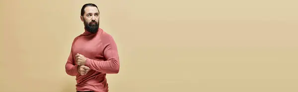 Serious good looking man with beard posing in pink turtleneck jumper on beige backdrop, banner — Stock Photo